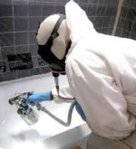 A technician wearing white protective clothes and a mask is resurfacing a bathtub.
