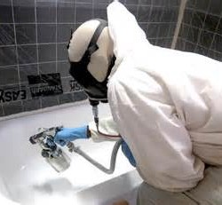 A technician wearing white protective clothes and a mask is resurfacing a bathtub.