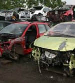 Auto scrap yard showing a red and a green cars that were in an accident