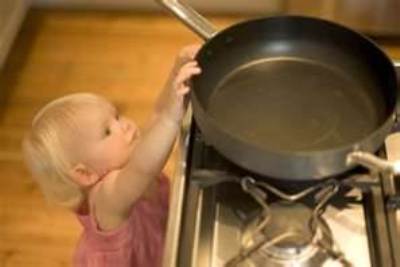 Little girl reaching for a frying pan on a stove
